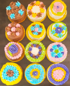 Assortment of colorful bunt cakes decorated with intricate floral designs in various colors, created by Cake Coma.